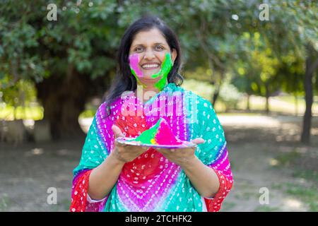 Glückliche indianerin, die weiße Kurta trägt und Farbpulver oder gulal hält. Wir feiern das holi-Festival im Park oder Garten. Stockfoto