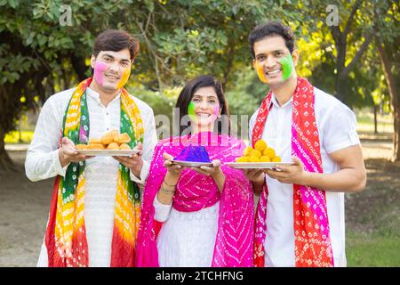 Glückliche Gruppe von drei indianern, die weiße Kurta tragen und bunte Farbe oder gulalplatte in den Händen halten, um das holi-Festival im Park oder in der Garde zu feiern Stockfoto