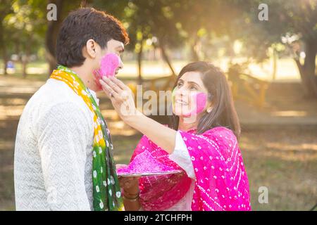 Glückliches, junges indisches Paar, das weiße Kurta spielt und Farbe ins Gesicht bringt. Feiern Sie gemeinsam holi im Freien im Park oder Garten. Stockfoto