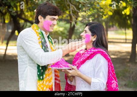 Glückliches, junges indisches Paar, das weiße Kurta spielt und Farbe ins Gesicht bringt. Feiern Sie gemeinsam holi im Freien im Park oder Garten. Stockfoto