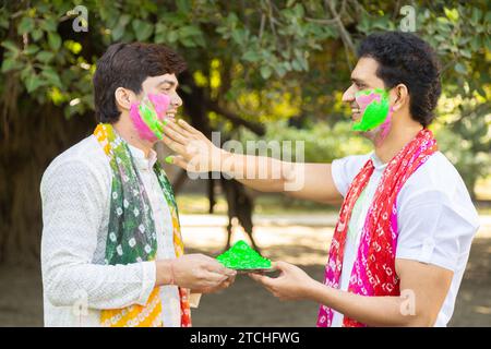 Zwei junge indische Freunde, die weiße Kurta spielen und Farbe ins Gesicht zaubern. Feiern Sie gemeinsam holi im Freien im Park oder Garten. Stockfoto