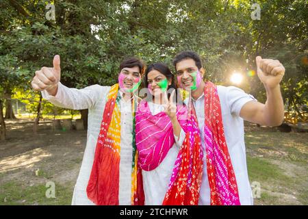 Eine Gruppe von drei indianern, die weiße Kurta tragen, feiert das holi-Festival im Park im Freien mit farbenfroher Farbe oder gulal auf ihren Gesichtern Stockfoto