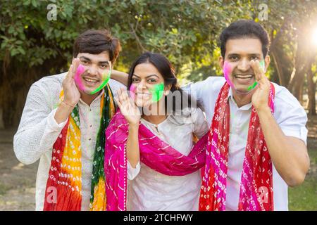 Eine Gruppe von drei indianern, die weiße Kurta tragen, feiert das holi-Festival im Park im Freien mit farbenfroher Farbe oder gulal auf ihren Gesichtern Stockfoto