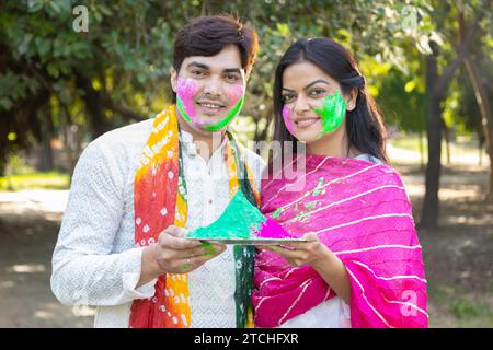 Glückliches, junges indisches Paar, das weiße Kurta spielt und Farbe ins Gesicht bringt. Feiern Sie gemeinsam holi im Freien im Park oder Garten. Stockfoto