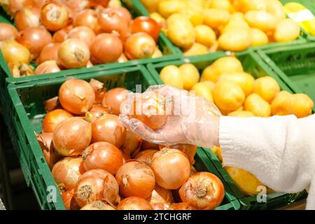 Nahaufnahme einer nicht erkennbaren Frau, die Zwiebeln in einem Lebensmittelgeschäft pflückt, aus persönlicher Perspektive. Stockfoto