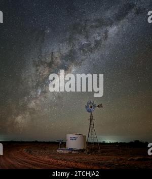 Der Milchstraßenkern erhebt sich über einer windbetriebenen Wasserpumpe auf einer Viehstation in Westaustralien Stockfoto