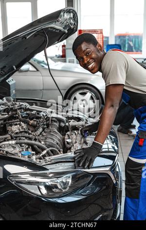 Junger afrikanischer Mann, der unter der Motorhaube eines Autos arbeitet, der den Motor im Autodienst repariert Stockfoto