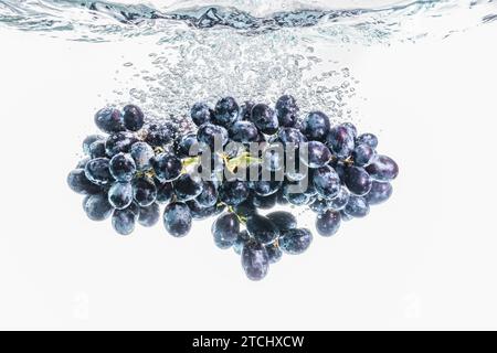 Rote Trauben, die auf dem Hintergrund in kristallklares Wasser spritzen. Gesunde Ernährung Stockfoto