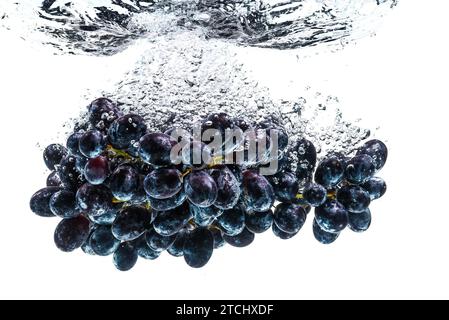 Rote Trauben, die auf dem Hintergrund in kristallklares Wasser spritzen. Gesunde Ernährung Stockfoto