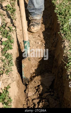 Ein Mann schaufelt einen Graben für Abwasser und Abwasser, aus nächster Nähe. Stockfoto