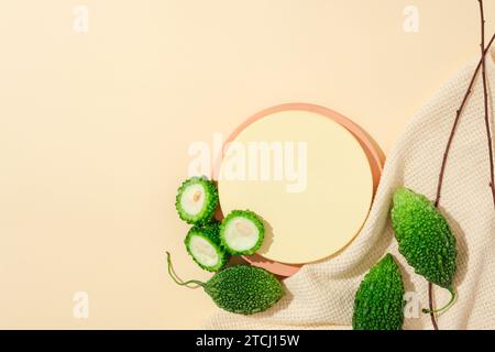 Frische Bittermelone ist um die runde Plattform mit Tuch und trockenen Zweigen verziert. Bittermelonen-Maske kann dazu beitragen, dass raue Haut wieder frisch wird. Natur Stockfoto
