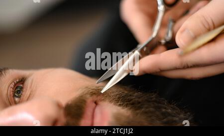 Ein Friseur-Stylist trimmt einem Kaukasier Schnurrbart mit einer Schere Stockfoto