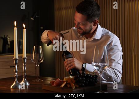 Romantisches Abendessen. Mann öffnet eine Weinflasche mit Korkenzieher am Tisch drinnen Stockfoto