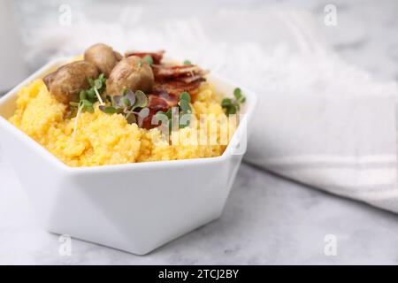 Gekochtes Maismehl mit Speck, Pilzen und Mikrogrün in Schüssel auf weißem Marmortisch, Nahaufnahme. Leerzeichen für Text Stockfoto