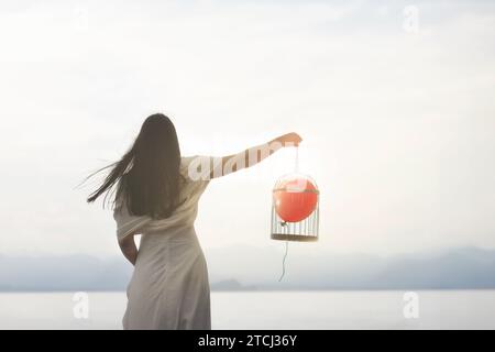 Eine surreale Frau geht, um ihren roten Ballon zu befreien, der gefangen im Käfig gehalten wird. Das Konzept, dass Wachstum erwachsen wird Stockfoto