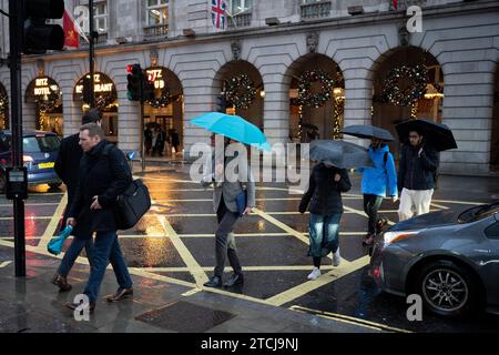 Weihnachtseinkäufer und andere Fußgänger überqueren Piccadilly an einem regnerischen Nachmittag in Westminster, am 12. Dezember 2023 in London, England. Stockfoto