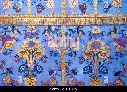 Fragment eines antiken Wandteppichs an einer verputzten Wand der Kirche des Heiligen Franziskus in Evora, Portugal. Muster mit goldenen Blumen und Blumenmotiven auf blu Stockfoto