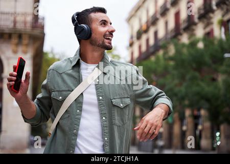 Junger kaukasischer Mann, der Spaß hat, während er Musik auf seinen Kopfhörern auf der Straße in der Stadt hört. Stockfoto