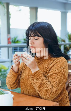 Junge lateinfrau, die mit geschlossenen Augen sitzt und das Aroma frisch gebrühten Kaffees genießt Stockfoto