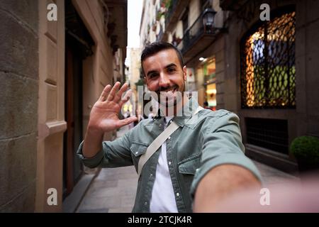 Junger Mann bei einem Videoanruf winkt der Kamera lächelnd zu. Stockfoto
