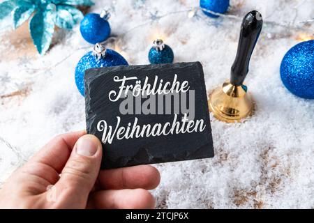 13. Dezember 2023: Handhaltetafel mit Aufschrift Frohe Weihnachten vor blauen Weihnachtskugeln und Weihnachtsdekorationen FOTOMONTAGE *** Handhaltetafel mit Aufschrift fröhliche Weihnachten vor blauen Christbaumkugeln und Weihnachtsdekoration FOTOMONTAGE Stockfoto