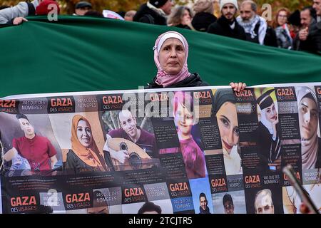 Marseille, Frankreich. Dezember 2023. Eine palästinensische Demonstrantin hält ein Banner, das Fotos mit den Namen der Opfer israelischer Bombenanschläge während der Demonstration zeigt. Die Demonstration für einen Waffenstillstand im Gazastreifen fand nach einer Entscheidung des Verwaltungsgerichts zunächst vom Polizeipräsidium Bouches-du-RhÃ wegen ernsthafter Gefahr einer Störung der öffentlichen Ordnung verboten statt. (Credit Image: © Gerard Bottino/SOPA Images via ZUMA Press Wire) NUR REDAKTIONELLE VERWENDUNG! Nicht für kommerzielle ZWECKE! Stockfoto