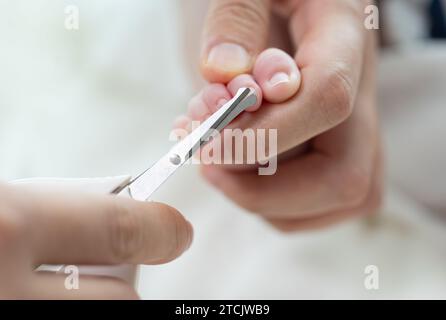 Mutterhände schneiden die Zehennägel des Neugeborenen mit einer Schere Stockfoto