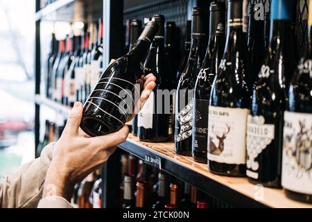 Kunde wählt eine Weinflasche aus dem Store-Regal. Eine Person, die eine Flasche aus einer vielfältigen Auswahl in einem gut sortierten Weinladen auswählt Stockfoto