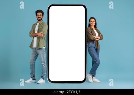 Positives junges indisches Paar, das am großen Handy steht, Mockup Stockfoto