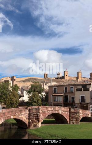 Eine Steinbrücke überspannt einen Fluss mit einer Burg mit mehreren Türmen im Hintergrund. Der Himmel ist blau mit weißen Wolken in molina de Argon Stockfoto