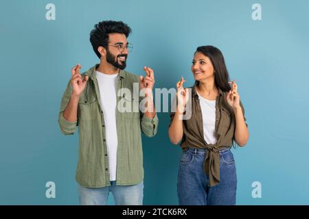 Glücklicher indischer Mann und Frau, die die Finger kreuzen, blauer Hintergrund Stockfoto