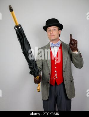 Porträt eines britischen Vintage-Gentleman in Tweed-Jacke und roter Weste mit Regenschirm, um die Aufmerksamkeit auf sich zu ziehen. Stockfoto