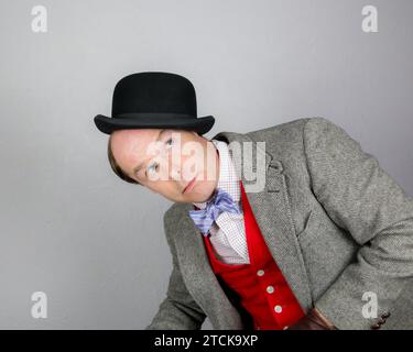 Porträt eines britischen Charakters in Tweed-Anzug und roter Weste, der einen Bowler-Hut auf seinem Kopf ausbalanciert. Konzept des Vintage Vaudeville Comic Schauspielers. Stockfoto