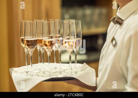 Ein junger Kellner hält einen Teller mit Champagner oder Prosecco als Begrüßungsgetränk bei einer Hotelveranstaltung. Stockfoto