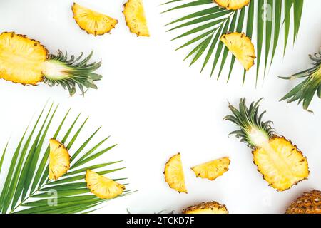 Tropischer Rahmen aus geschnittenen Ananas und Palmblättern auf weißem Hintergrund. Flache Lage, Draufsicht. Stockfoto
