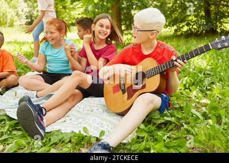 Behinderter Junge, der Gitarre spielt, während er sich mit Freunden während des Picknicks im Park auf eine Decke setzt Stockfoto