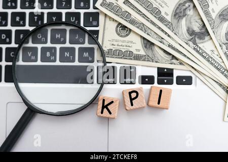 KPI ( Key Performance Indicator) – Akronym auf Holzwürfeln auf dem Hintergrund eines Kakteen und Banknoten. Geschäftskonzept Stockfoto