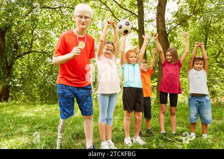 Ein behinderter Junge zeigt Medaille mit fröhlichen Freunden, die den Sieg im Park feiern Stockfoto