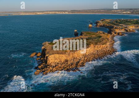 Luftbild der hochfelsigen Landzunge und Halbinsel. Drohnenfoto von blauen Wellen schlagen und plätschern im Sommer Sonnenuntergang, kleine Laubwälder und felsige Klippen, in Peniche, Portugal. Stockfoto