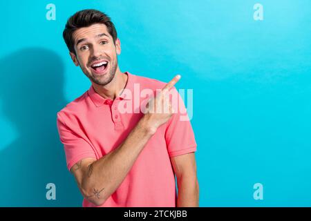 Foto des jungen gutaussehenden Mannes in rosa T-Shirt, der Finger-leeren Raum zeigt, der Tätowiersalon auf aquamarinfarbenem Hintergrund fördert Stockfoto