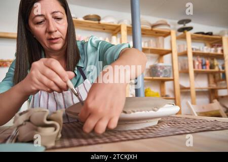 Eine engagierte Keramikerin perfektioniert ihre Arbeit in Ton und taucht in den künstlerischen Prozess in ihrer Werkstatt ein. Handwerkskunst Stockfoto