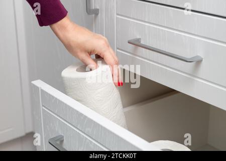 Frau, die Papierhandtuch aus der Küchenschublade herausnimmt. Die Hand nimmt ein Papiertuch heraus. Papiertuch in der Küche. Stockfoto