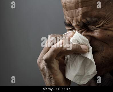 Mann, der die Erkältung und Grippe fängt Mann, der Nase bläst, nachdem er eine Erkältung mit grauem Hintergrund mit Leuten Stock Foto gefangen hat Stockfoto