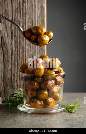Scharfe Oliven in einer Glasschale. Schüssel mit eingelegten Oliven und Rosmarinzweigen auf einem Steintisch. Stockfoto