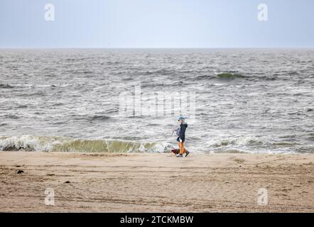 Eine Frau, die ihren Hund an einem bedeckten kühlen Tag an einem East hampton Beach begleitet Stockfoto