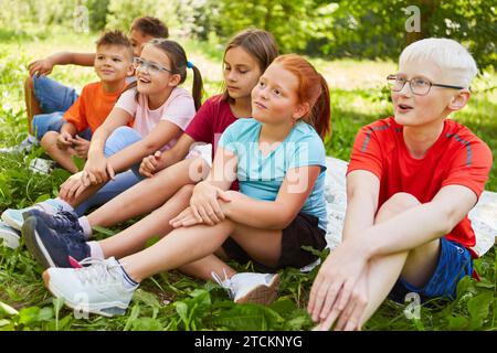Lächelnde männliche und weibliche Freunde, die wegschauen, während sie zusammen auf dem Gras im Park sitzen Stockfoto
