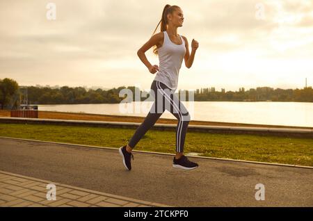 Junge schlanke sportliche Frau in Sportbekleidung, die im Park entlang des Flusses läuft. Stockfoto