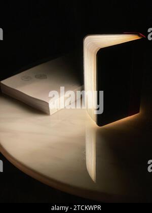 Ein Nahbild einer beleuchteten Computermaus und eines offenen Buches, das auf einem dunklen Holztisch liegt Stockfoto