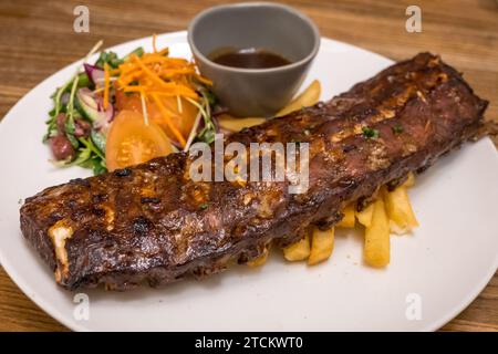 Gegrillte saftige Schweinerippchen vom Grill auf einem weißen Teller mit Pommes frites und Salat in Adelaide, Australien Stockfoto