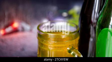 Ein Getränkekonzept mit einem Bier und Flaschen Bier und einem Bild eines abgestürzten Autos im Hintergrund. Stockfoto